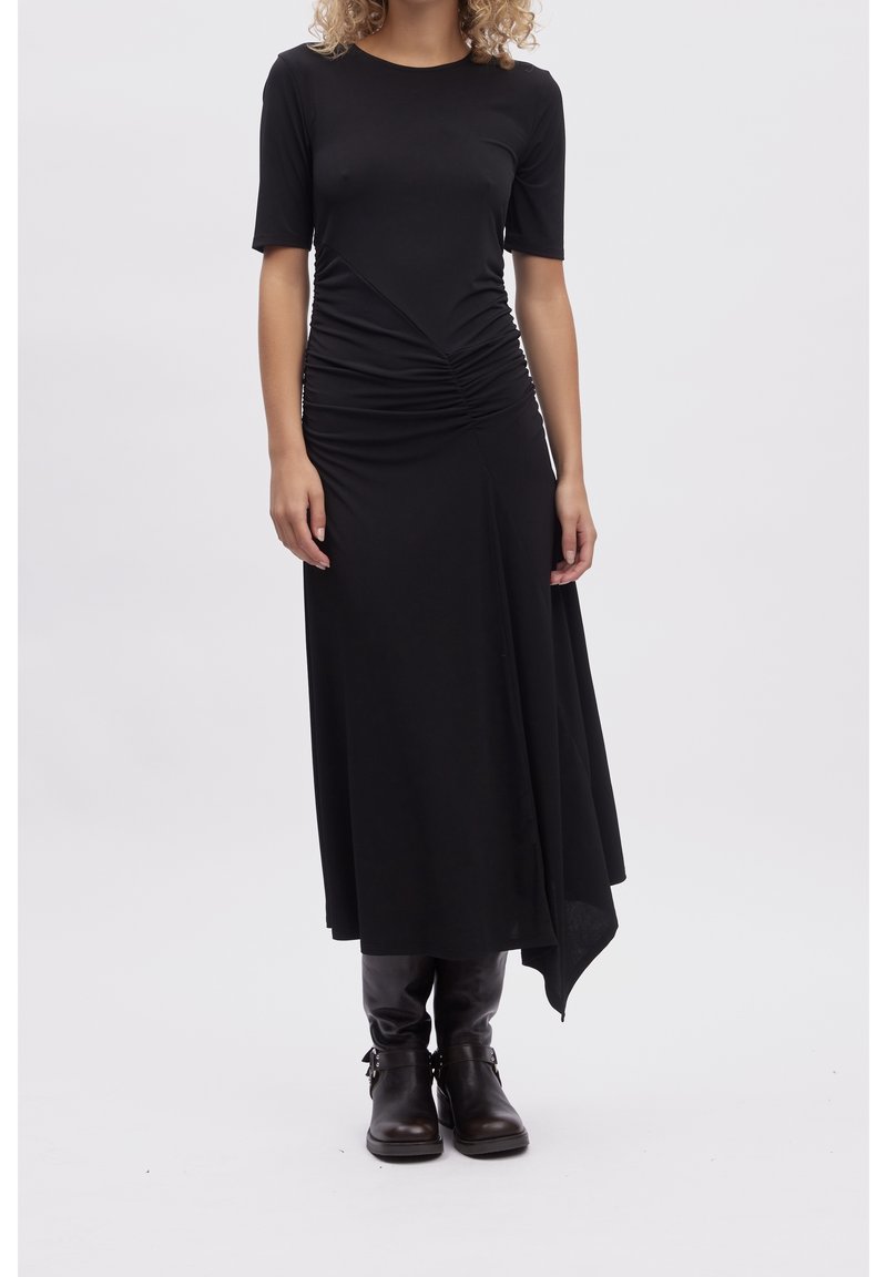 Robe noire longueur genou en tissu lisse. Caractérisée par des manches courtes et des fronces à la taille, avec un ourlet asymétrique.