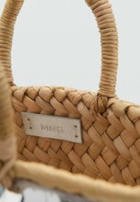 Sac en osier tressé couleur beige avec une finition texturée, des poignées circulaires et une petite étiquette en cuir embossée avec "MNG". L'intérieur est spacieux et naturel.