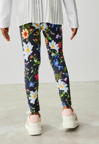Blommiga leggings har en mörk bakgrund med livfulla blommor i olika färger. Outfiten matchas med vita sneakers med rosa detaljer.