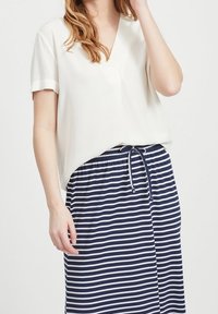 Blouse blanche à manches courtes avec encolure en V et poignets retroussés, associée à une jupe à taille élastiquée à cordon, rayée bleu marine et blanc.