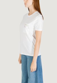 Camiseta blanca de algodón con cuello redondo, mangas cortas y un bolsillo en la parte delantera que presenta patrones decorativos en forma de lágrima en colores pastel.