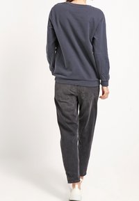 Felpa blu navy con collo a giro, vestibilità comoda e polsini a costine; abbinata a jeans grigi con taglio largo e due tasche posteriori.