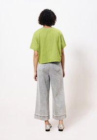 Groene cropped t-shirt van katoen, gecombineerd met lichtgrijze denim jeans met hoge taille en wijde pijen, voorzien van rafelige zomen en zakken.