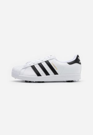 Hvid Adidas Superstar sneakers med sorte striber og hælkappe, gyldent "SUPERSTAR"-tryk og sål med knopper for greb.