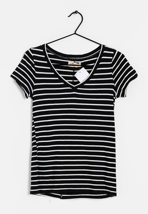 Czarna i biała koszulka w poziome paski z krótkim rękawem i dekoltem w serek, wisząca na czarnym wieszaku z dołączoną białą metką.