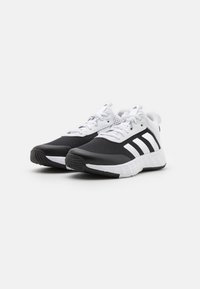 Des chaussures de sport en noir et blanc avec une tige en mesh, trois rayures blanches sur le côté et une semelle texturée pour l'adhérence.