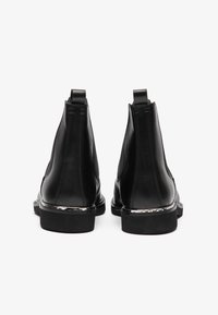 Botas de tobillo de cuero negro con paneles laterales elásticos, tiradores traseros y una suela texturizada. Presentan un sutil toque metálico en el tacón.