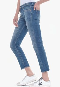 Vaqueros de denim azul con corte slim, con una cintura de altura media, un desvanecimiento sutil y dobladillos acampanados, combinados con zapatillas blancas.