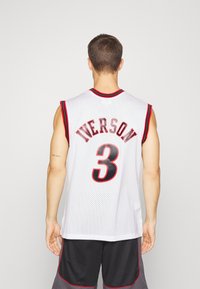 Mies joka katsoo poispäin, päällään valkoinen koripallopaita, jossa lukee "Iverson" ja numero 3 mustalla ja punaisella, yhdistettynä mustiin ja harmaisiin shortseihin.