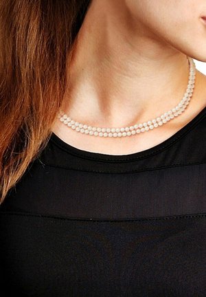 Deux brins de petites perles rondes et translucides aux teintes pastel douces, portés autour du cou, sur un haut noir. Design de fermoir simple.