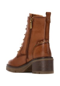 Botín de cuero marrón hasta el tobillo con cremallera lateral, parte frontal con cordones, detalles en dorado, tacón texturizado y una suela de goma robusta y contorneada.