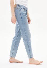 Jeans de denim azul claro con corte recto, cinco bolsillos y un parche de cuero en la cintura. La tela parece ligeramente desgastada con una textura suave.