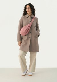 Hnědý vlněný kabát s velkými knoflíky, kombinovaný se světle béžovými kordovými širokými kalhotami a růžovou crossbody taškou. Bílé tenisky dokreslují celý outfit.