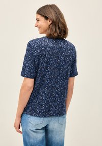 Modrá košile s krátkým rukávem s vzorem listů na námořnickém pozadí. Měkká tkanina, uvolněný střih a neformální design vhodný pro každodenní nošení.