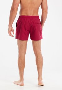 Rode zwemshorts van lichtgewicht stof, met een elastische tailleband, zijzakken en een enkele achterzak met een klein logo-detail.