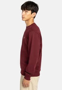 Bordeaux sweatshirt med rund halsudskæring, ribbede ærmer og kant. Glat tekstur, har et lille logo på brystet.