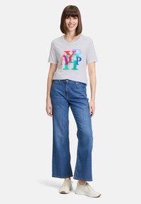 Lichtgrijze t-shirt met kleurrijke grafische letters, gecombineerd met wijde blauwe jeans en crèmekleurige sneakers. Soepele stof, casual pasvorm.