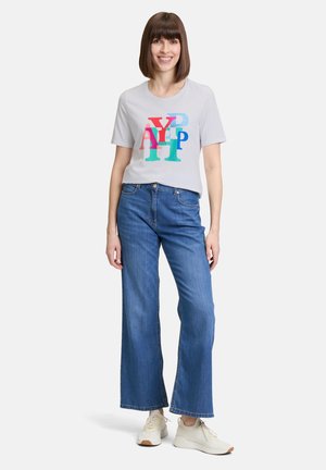 T-shirt gris clair avec des lettres graphiques colorées, associé à un jean bleu à jambes larges et des baskets crème. Tissu lisse, coupe décontractée.
