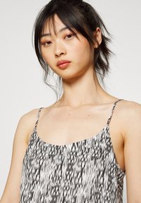 Vestido sem mangas em preto e branco com um design fluido, apresentando um padrão marmoreado e alças finas. Tecido suave com uma leve textura.