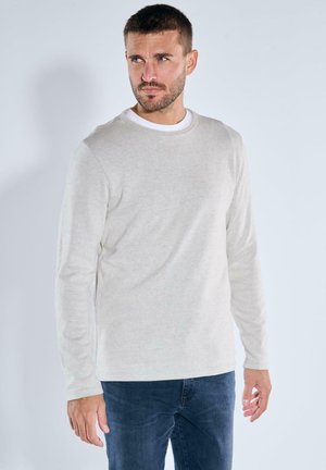 Hellegraues Langarmshirt aus weichem Stoff, mit Rundhalsausschnitt und klaren Linien, kombiniert mit dunkelblauen Jeans.