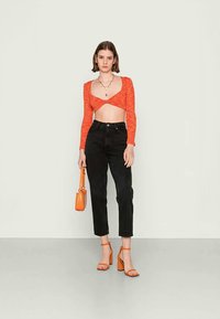 Top laranja cropped com mangas longas, jeans pretos de cintura alta, sandálias laranjas de salto e uma pequena mala laranja.