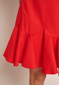 Sarkans flared kleita, izgatavota no kokvilnas, ar viļņotu apakšmalu. Tai ir gluda tekstūra un leņķveida šuves ap vidukli.