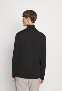 Camiseta negra de manga larga con cuello alto, de diseño ajustado, textura suave y cuello plano. Estilo simple y minimalista sin patrones.