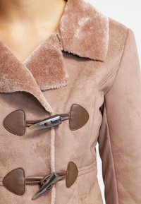 Lyserød faux suede frakke med en blød krave, der har brune toggles og detaljer. Glat tekstur og skræddersyet pasform med synlige sømme.