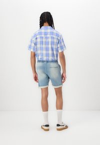 Koszula w kratę w kolorze jasnoniebieskim i fioletowym z krótkim rękawem, w połączeniu z wyblakłymi szortami dżinsowymi z elastycznym pasem i podwiniętymi rękawami.