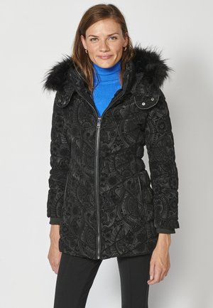 Schwarze gepolsterte Jacke mit Muster und einer Kapuze aus Kunstfell, Reißverschluss und gerippten Bündchen, die auf dem Stoff aufwendige Designs bietet.