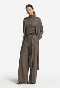 Brun ribbad polokrage under en lång, öppen cardigan. Vida mönstrade byxor med bälte i midjan. Bruna spetsiga skor fulländar outfiten.