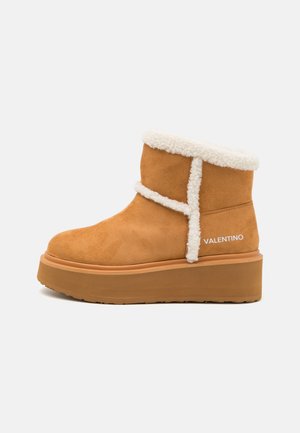 Botine din suede bej cu captuseala din blana ecologica crema, detalii pe cusatura laterala si talpa groasa. Prezinta o marca discreta alba pe lateral.