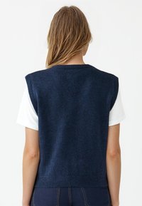 Maglione maniche corte in maglia blu navale con scollo rotondo e orlo a coste, abbinato a una camicia bianca a maniche corte sotto.