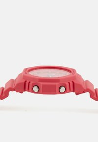 Rdeča plastična ura s krožno površino, dvema stranskima gumboma in teksturiranim pasom. Ima prozorno številčnico in izrazite oznake ur.
