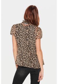 Durchsichtige braune Bluse mit Leopardenmuster, kurzen Puffärmeln, gerafftem Ausschnitt und lockerer Passform, kombiniert mit schwarzen Jeans.