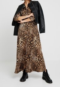 Abito maxi con stampa leopardata, maniche lunghe, frontale con bottoni e spacco laterale, abbinato a una giacca di pelle nera e stivali neri alla caviglia.
