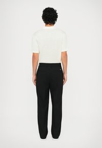 White, short-sleeved shirt with a crew neck; paired with black, loose-fitting pants. Both garments have a smooth texture.