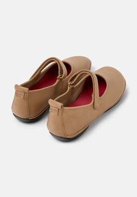 Brązowe skórzane buty typu Mary Jane z okrągłym noskiem, z wycięciem i czerwonym wnętrzem. Posiadają niski obcas oraz akcent z logo z tyłu.