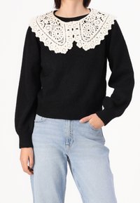 Pull noir avec des manches volumineuses et un large col en dentelle blanche. Le matériau semble doux, avec un ourlet et des poignets côtelés.