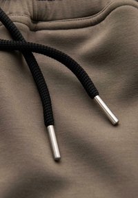 Zbliżenie na czarne sznurki od bluzy z kapturem z srebrnymi metalowymi końcówkami leżące na taupe'owym materiale.