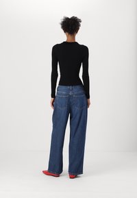 Haut noir à manches longues à côtes associé à un jean en denim bleu ample et des chaussures rouges. Remarque : poches arrière visibles et détails de couture contrastés.