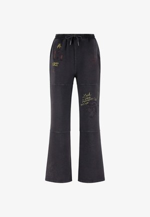 Pantalones de chándal negros con cintura ajustable, con varios estampados gráficos en amarillo y rojo, diseño de pierna acampanada y costuras en contraste.