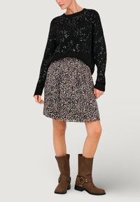 Pull en sequins noirs, superposé sur une jupe beige à imprimé léopard, associé à des bottines brunes avec des sangles et des éléments en argent.