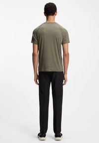 Oliwkowa zielona koszulka z krótkim rękawem, miękka tkanina, zaokrąglony dekolt, przeszycia na ramionach. Noszona z czarnymi, dopasowanymi spodniami i trampkami.