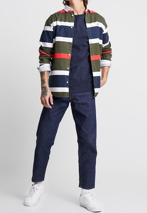 Raidallinen napillinen paita vihreän, laivastonsinisen, valkoisen ja punaisen sävyissä; yhdistetty tummansinisiin farkkuihin ja valkoisiin tennareihin. Puuvillamateriaalia, rento istuvuus.