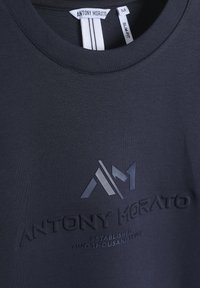 Camiseta ajustada de color azul marino oscuro con una textura suave, logo en relieve y un estampado sutil con el nombre de la marca y el año de establecimiento.