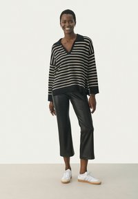 Zwart en beige gestreepte oversized trui met een v-hals, gecombineerd met zwarte gemodificeerde leren broek en witte sneakers.
