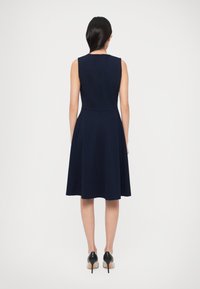 Námornícka modrá bezrukávová šaty s priliehavým živôtikom a rozšírenou sukňou, vyrobené z hladkej látky. Má čistý výstrih a zips na chrbte.