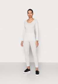 Top de manga longa cinza claro e leggings ajustadas em tecido texturizado, combinados com ténis pretos. Design simples com decote redondo.