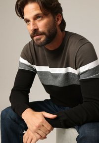 Pull en mélange de laine avec des rayures horizontales en gris charbon, blanc et noir. Il dispose d'un col rond et de manches longues.